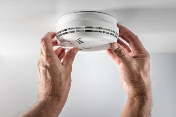 Hand installing a modern smart smoke detector on the ceiling for enhanced home safety.